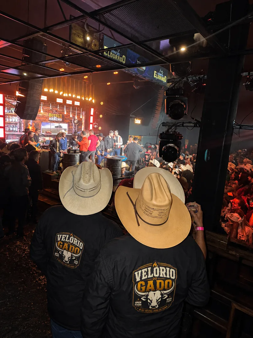 Público do Velório do Gado de jaqueta do evento, à noite, sob as luzes do rancho